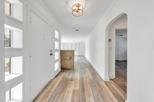 hall with light wood finished floors, arched walkways, crown molding, and baseboards