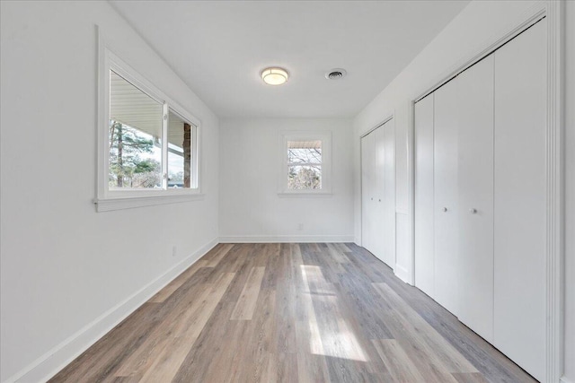 unfurnished bedroom with light wood finished floors, visible vents, baseboards, and multiple closets