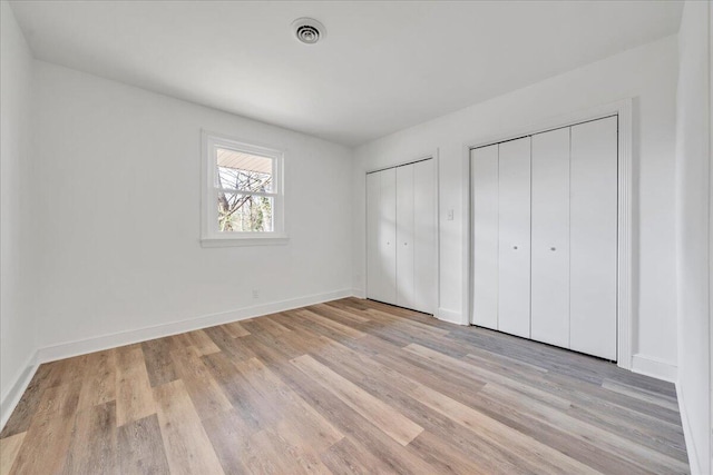 unfurnished bedroom featuring light wood finished floors, visible vents, baseboards, and multiple closets