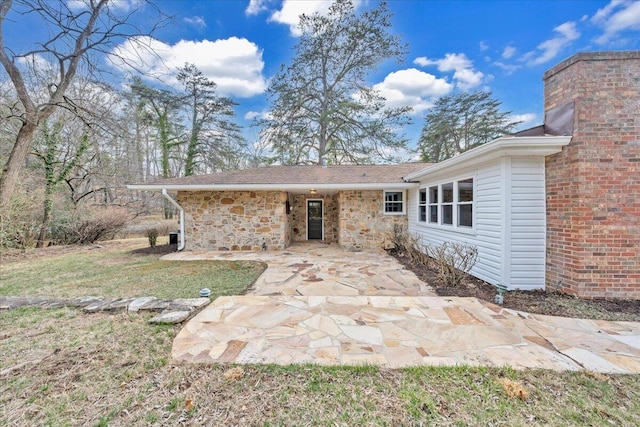 rear view of house featuring a patio area, stone siding, and a lawn