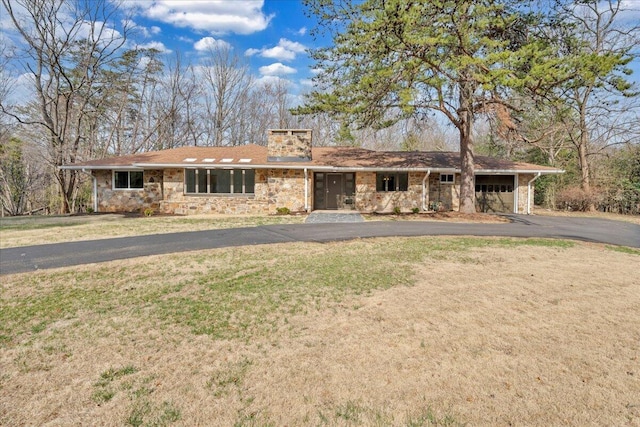 ranch-style home with aphalt driveway, a front yard, a chimney, stone siding, and an attached garage