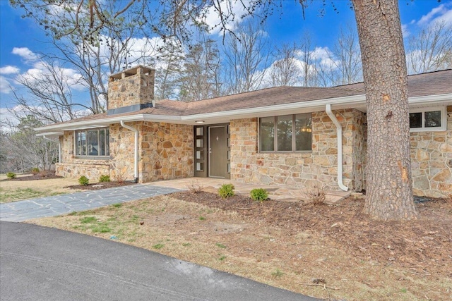 view of front of house with stone siding and a chimney