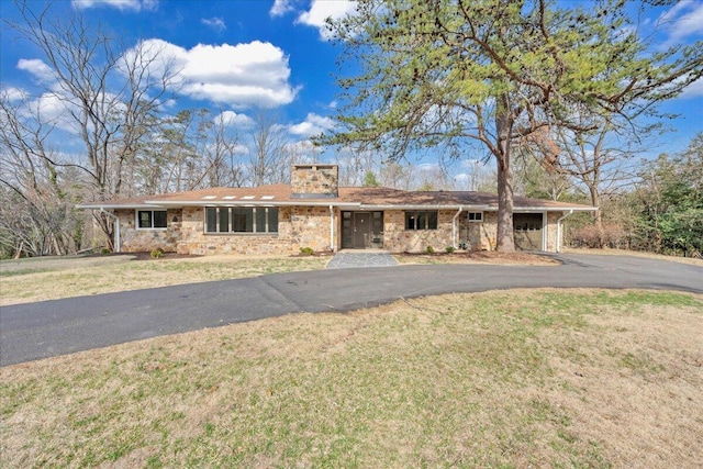 ranch-style house featuring a front lawn, a garage, stone siding, and driveway