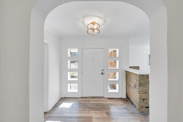 foyer entrance with arched walkways, wood finished floors, and ornamental molding