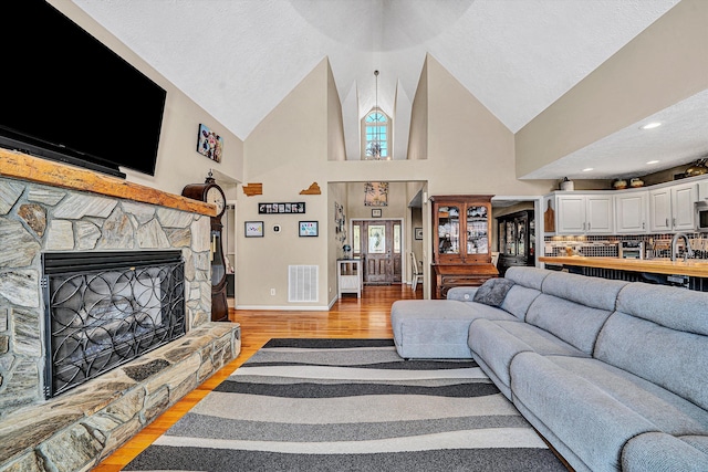 living room with high vaulted ceiling, visible vents, a fireplace, and light wood-style flooring