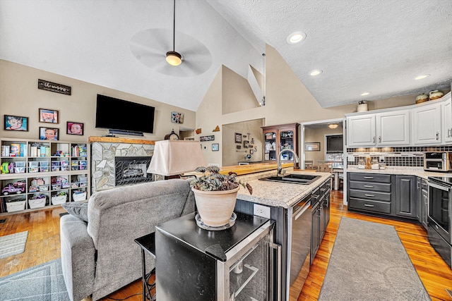 kitchen with a stone fireplace, a sink, white cabinetry, vaulted ceiling, and light wood finished floors