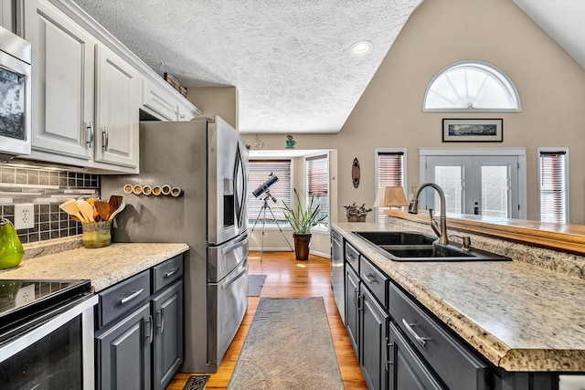 kitchen with lofted ceiling, stainless steel appliances, a sink, white cabinetry, and light wood finished floors