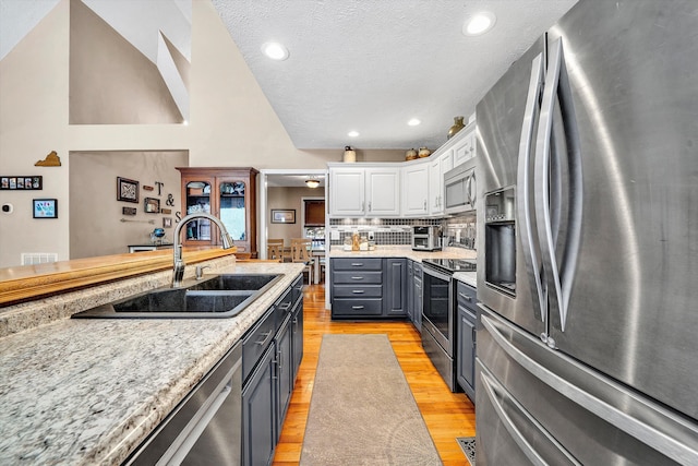 kitchen featuring gray cabinetry, stainless steel appliances, a sink, white cabinetry, and light wood-type flooring