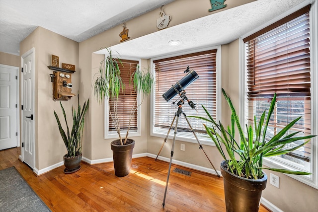 interior space featuring a textured ceiling, hardwood / wood-style flooring, visible vents, and baseboards