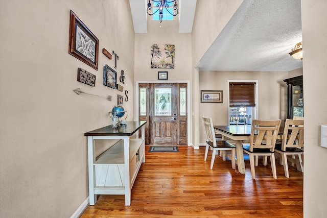 entryway with a textured ceiling, a towering ceiling, baseboards, and wood finished floors