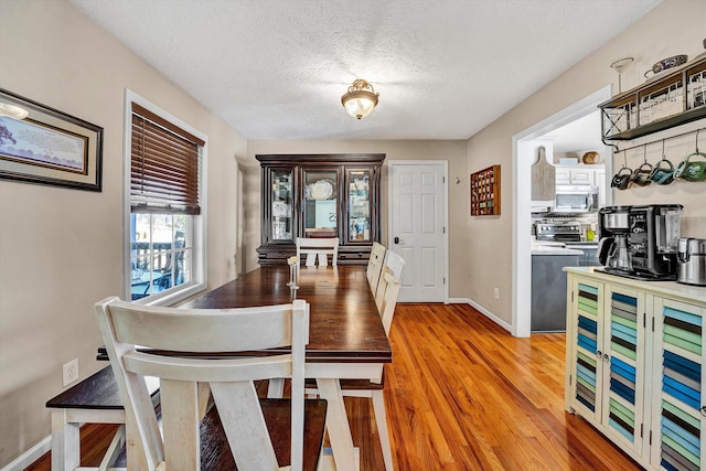 dining room featuring light wood finished floors, baseboards, and a textured ceiling