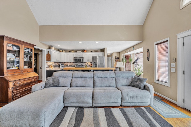 living room with light wood-type flooring, vaulted ceiling, baseboards, and recessed lighting