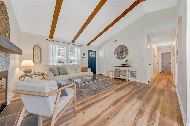 living room with visible vents, baseboards, a stone fireplace, wood finished floors, and high vaulted ceiling