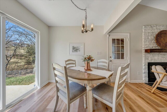 dining area with a stone fireplace, baseboards, light wood finished floors, and a chandelier