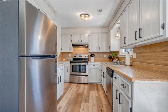 kitchen featuring tasteful backsplash, under cabinet range hood, light countertops, light wood-style flooring, and stainless steel appliances