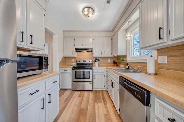 kitchen featuring a sink, decorative backsplash, light countertops, under cabinet range hood, and appliances with stainless steel finishes