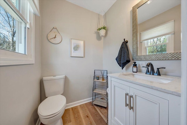 half bathroom featuring toilet, vanity, baseboards, and wood finished floors