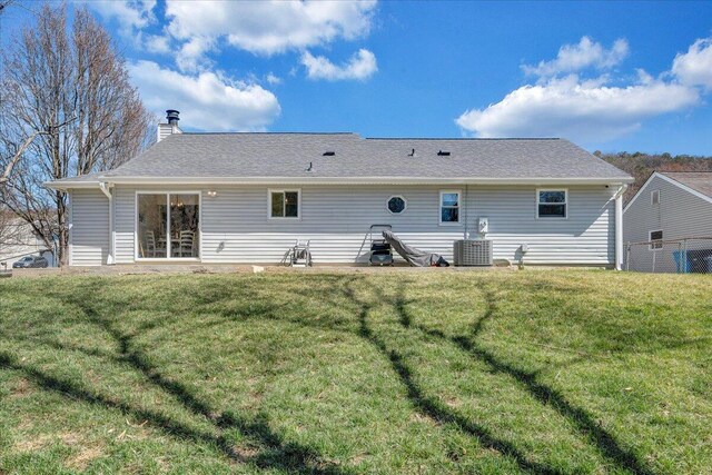 back of property featuring a lawn, cooling unit, a chimney, and a shingled roof