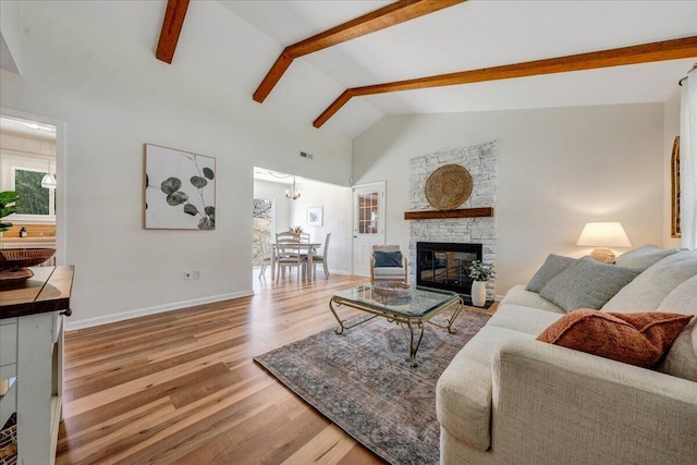 living area featuring visible vents, beam ceiling, wood finished floors, a stone fireplace, and baseboards