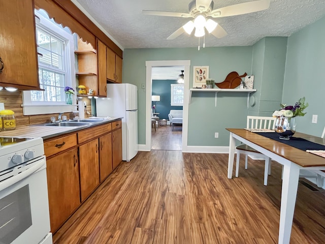 kitchen featuring open shelves, a textured ceiling, wood finished floors, white appliances, and brown cabinetry