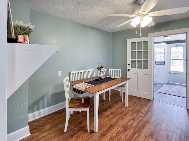 dining space with ceiling fan, a textured ceiling, baseboards, and wood finished floors