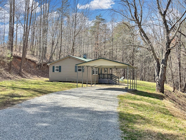 view of front of house with gravel driveway, a front yard, a wooded view, and a detached carport