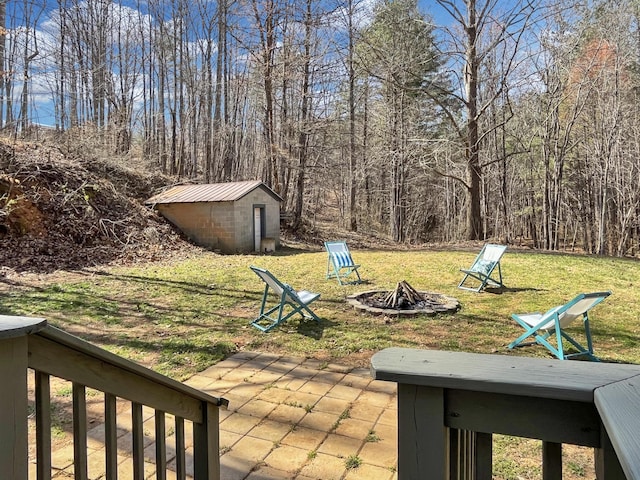 view of yard featuring an outbuilding, a patio, a forest view, a shed, and a fire pit