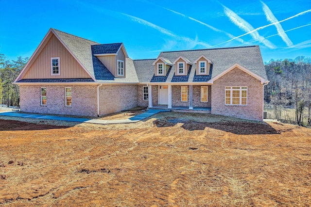 view of front of property featuring covered porch, brick siding, and roof with shingles