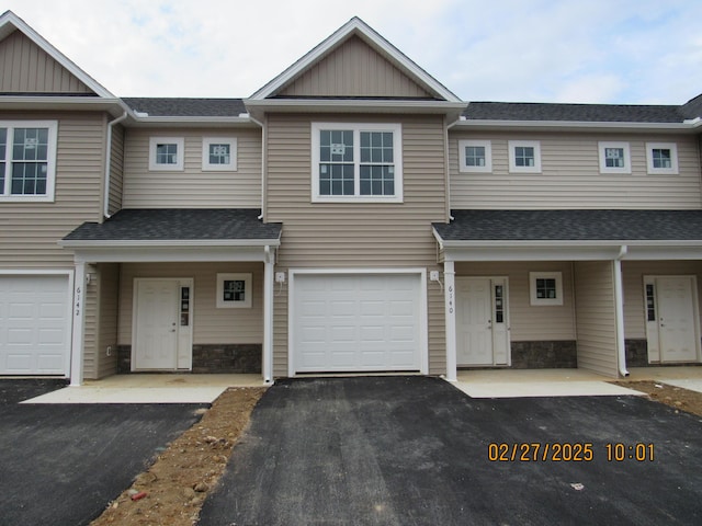 townhome / multi-family property featuring a garage, stone siding, roof with shingles, and aphalt driveway