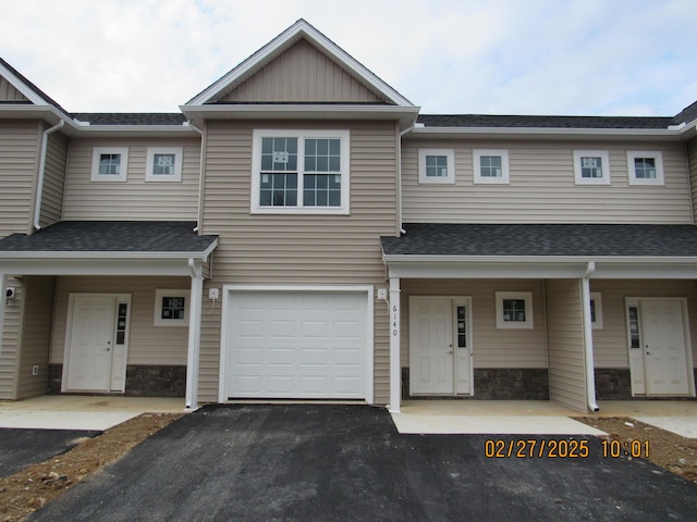 multi unit property with a garage, stone siding, roof with shingles, and aphalt driveway