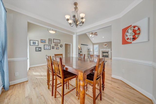 dining room featuring baseboards, ornamental molding, vaulted ceiling, light wood-type flooring, and a fireplace