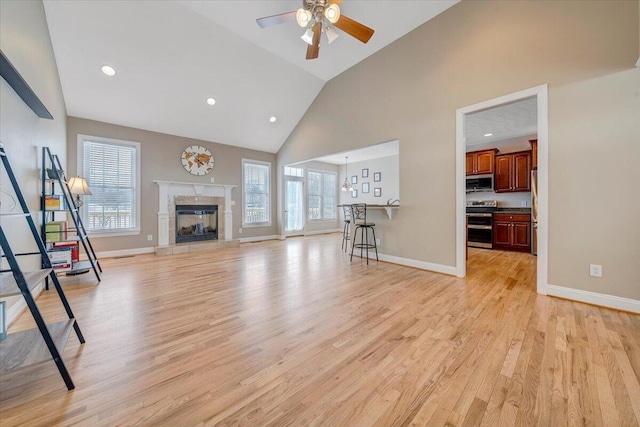 unfurnished living room with light wood-style floors, plenty of natural light, high vaulted ceiling, and baseboards