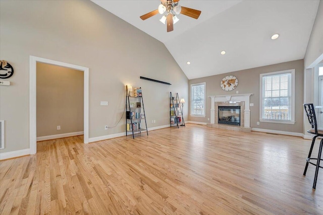 unfurnished living room featuring baseboards, a ceiling fan, a premium fireplace, light wood-type flooring, and high vaulted ceiling