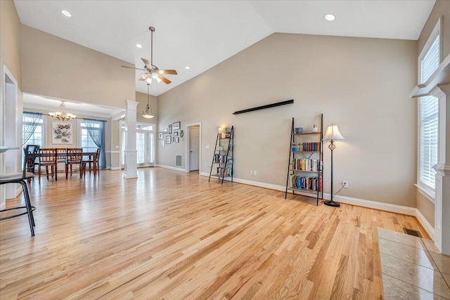 unfurnished living room featuring ornate columns, visible vents, high vaulted ceiling, light wood-type flooring, and baseboards