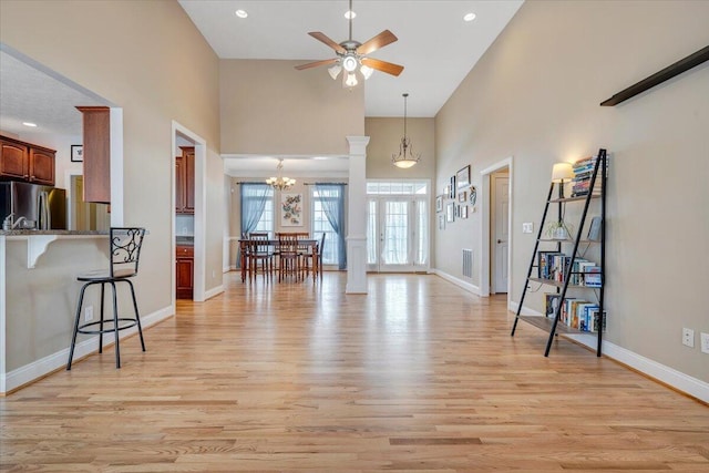 living area with recessed lighting, light wood-style flooring, a high ceiling, baseboards, and ceiling fan with notable chandelier