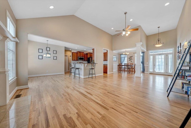 unfurnished living room with decorative columns, visible vents, light wood-type flooring, high vaulted ceiling, and ceiling fan with notable chandelier