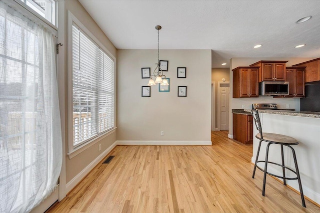 kitchen featuring pendant lighting, stainless steel microwave, visible vents, light wood-style flooring, and baseboards