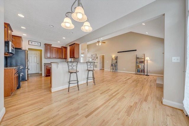 kitchen with brown cabinetry, light wood-style flooring, a breakfast bar area, open floor plan, and vaulted ceiling