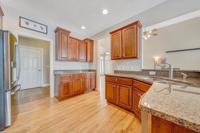 kitchen featuring light stone counters, stainless steel refrigerator with ice dispenser, light wood-style flooring, a sink, and a textured ceiling