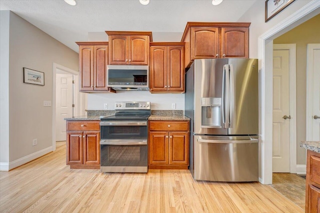 kitchen with light stone counters, stainless steel appliances, baseboards, light wood-type flooring, and brown cabinets