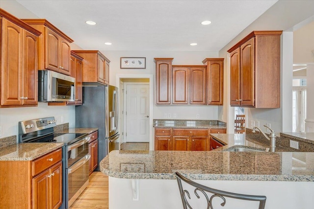 kitchen with a breakfast bar area, a sink, appliances with stainless steel finishes, light stone countertops, and light wood finished floors