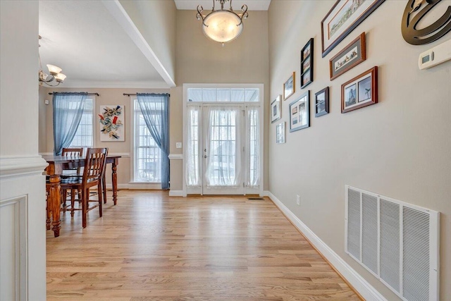 entrance foyer featuring baseboards, visible vents, a towering ceiling, an inviting chandelier, and light wood-type flooring