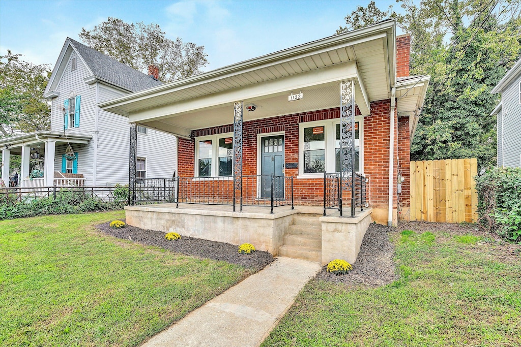 view of front of home featuring brick siding, a porch, fence, and a front yard