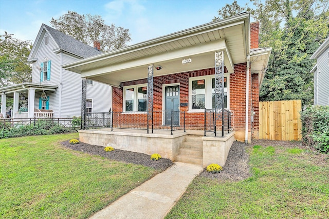 view of front of home featuring brick siding, a porch, fence, and a front yard