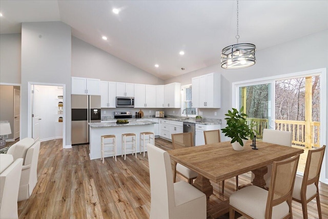 kitchen featuring high vaulted ceiling, a center island, white cabinets, light wood-style flooring, and appliances with stainless steel finishes