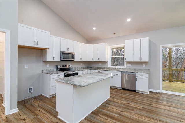 kitchen featuring appliances with stainless steel finishes, white cabinetry, a kitchen island, a sink, and wood finished floors