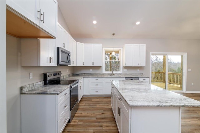 kitchen featuring appliances with stainless steel finishes, white cabinets, a kitchen island, a sink, and light stone countertops