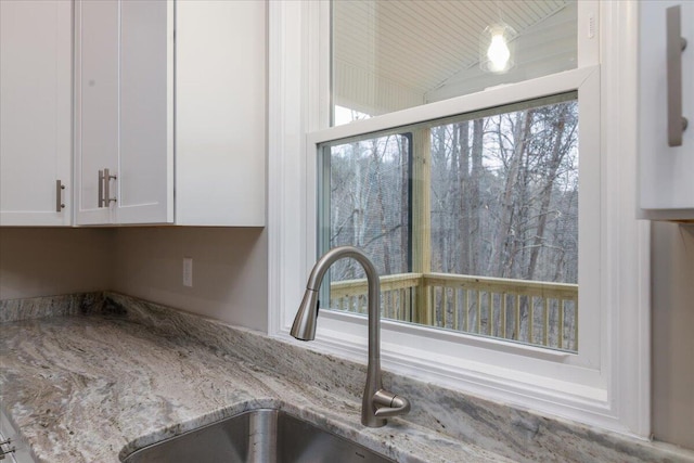 interior details with light stone counters, a sink, and white cabinets