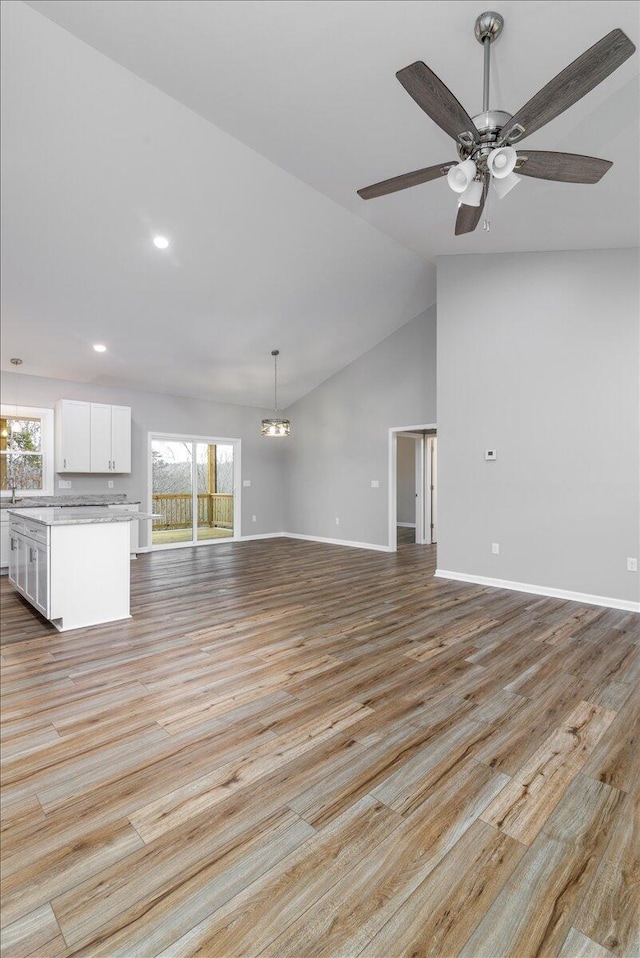 unfurnished living room with baseboards, lofted ceiling, light wood finished floors, and ceiling fan with notable chandelier