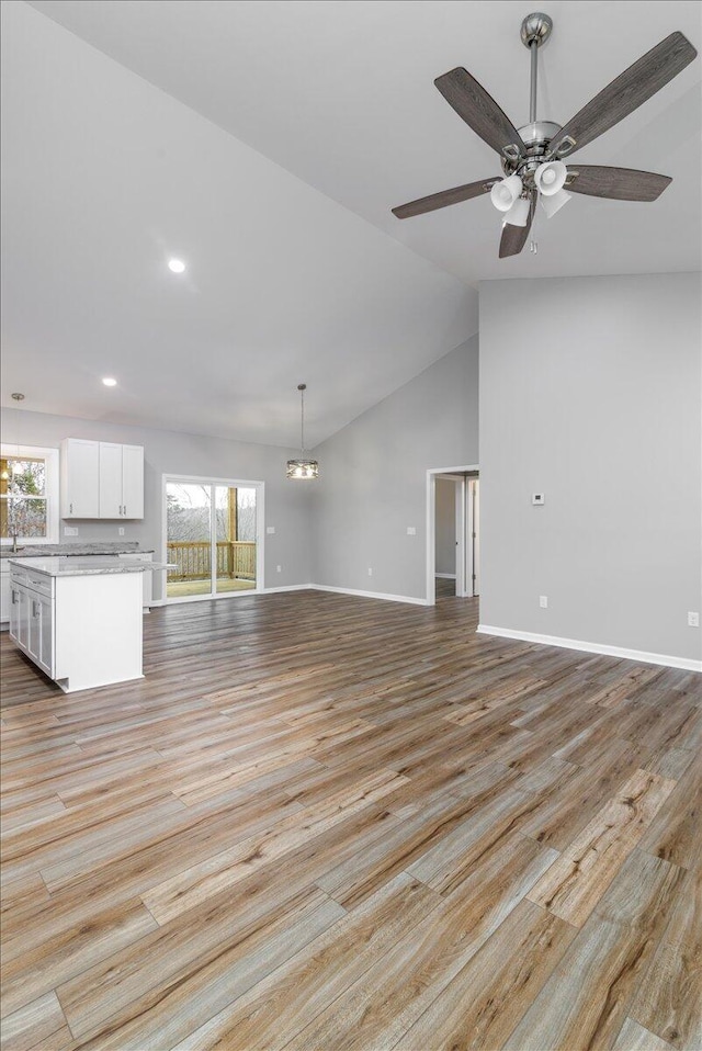 unfurnished living room featuring lofted ceiling, ceiling fan with notable chandelier, light wood-style flooring, and baseboards